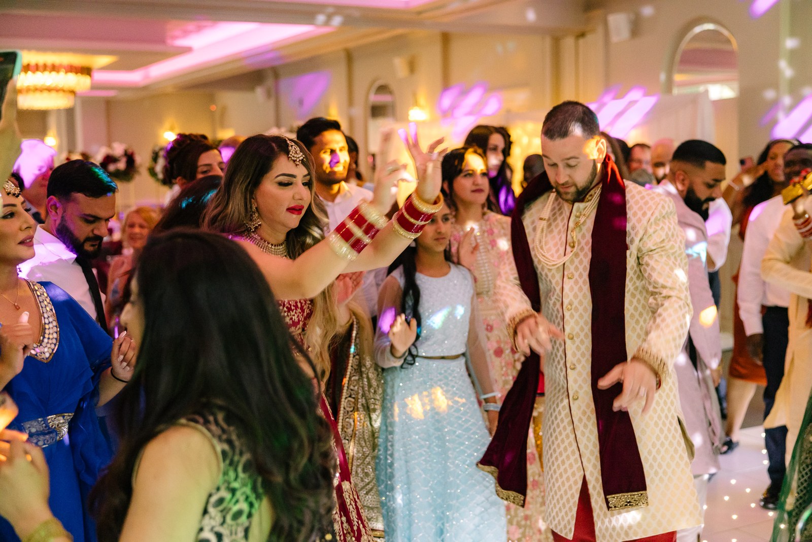 Guests filling the reception dance floor around the couple under pink lights