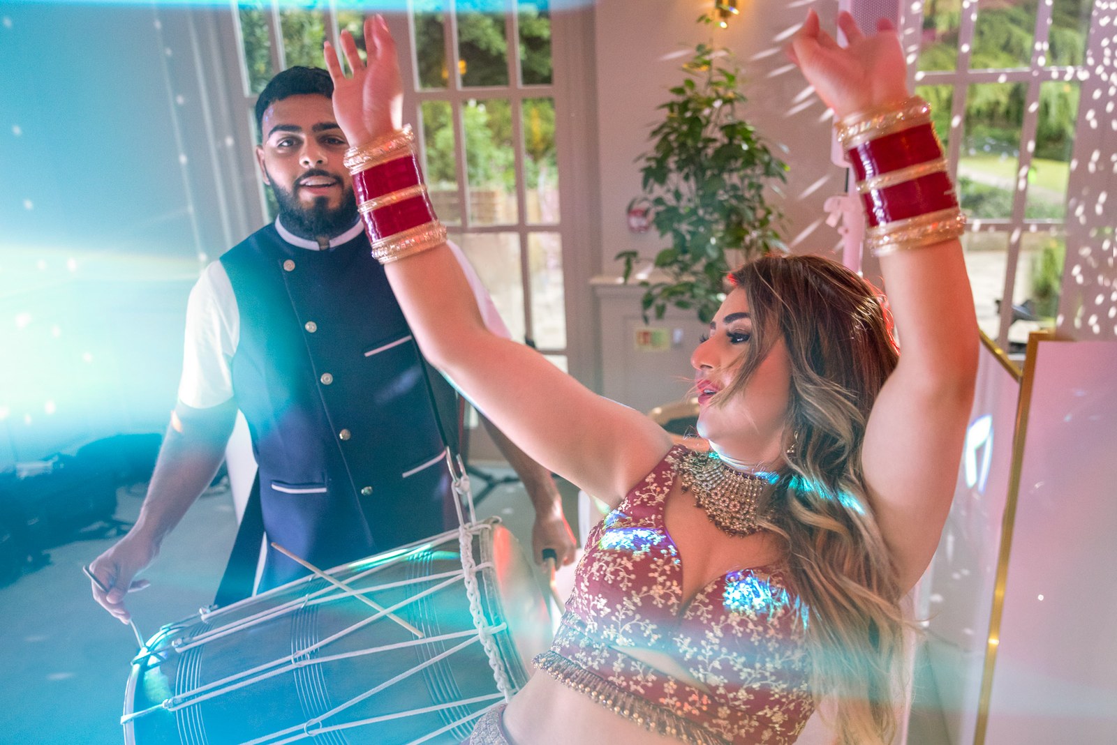A dhol drummer and the bride dance energetically under dramatic lighting