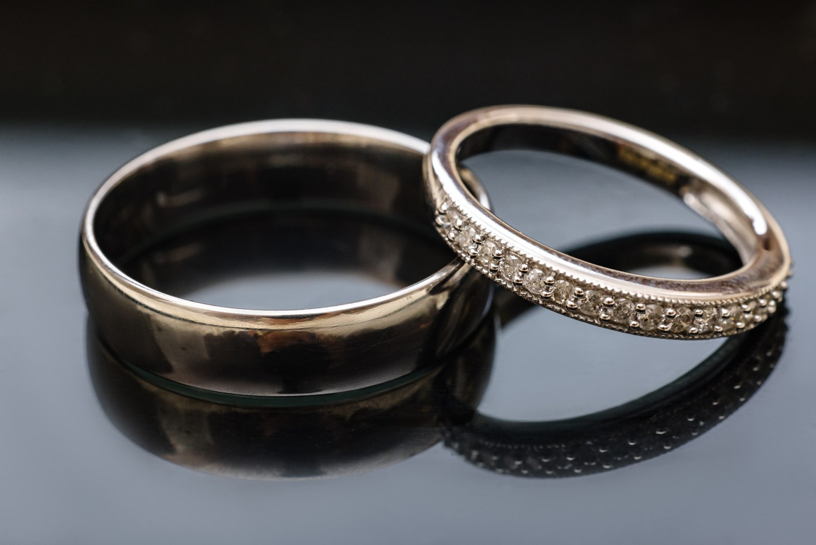 Close-up of the plain and diamond-set wedding rings on a dark reflective surface