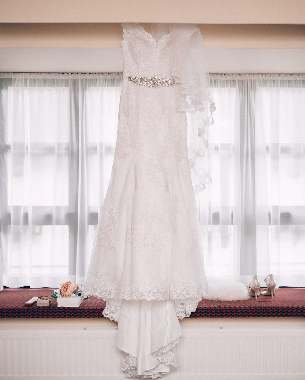 The bride's lace fishtail gown hanging at the window with her heels on the sill