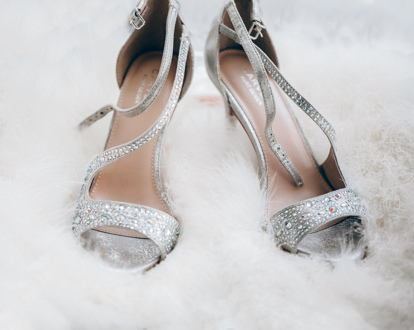 A pair of sparkling diamante strappy heels resting on soft white fur