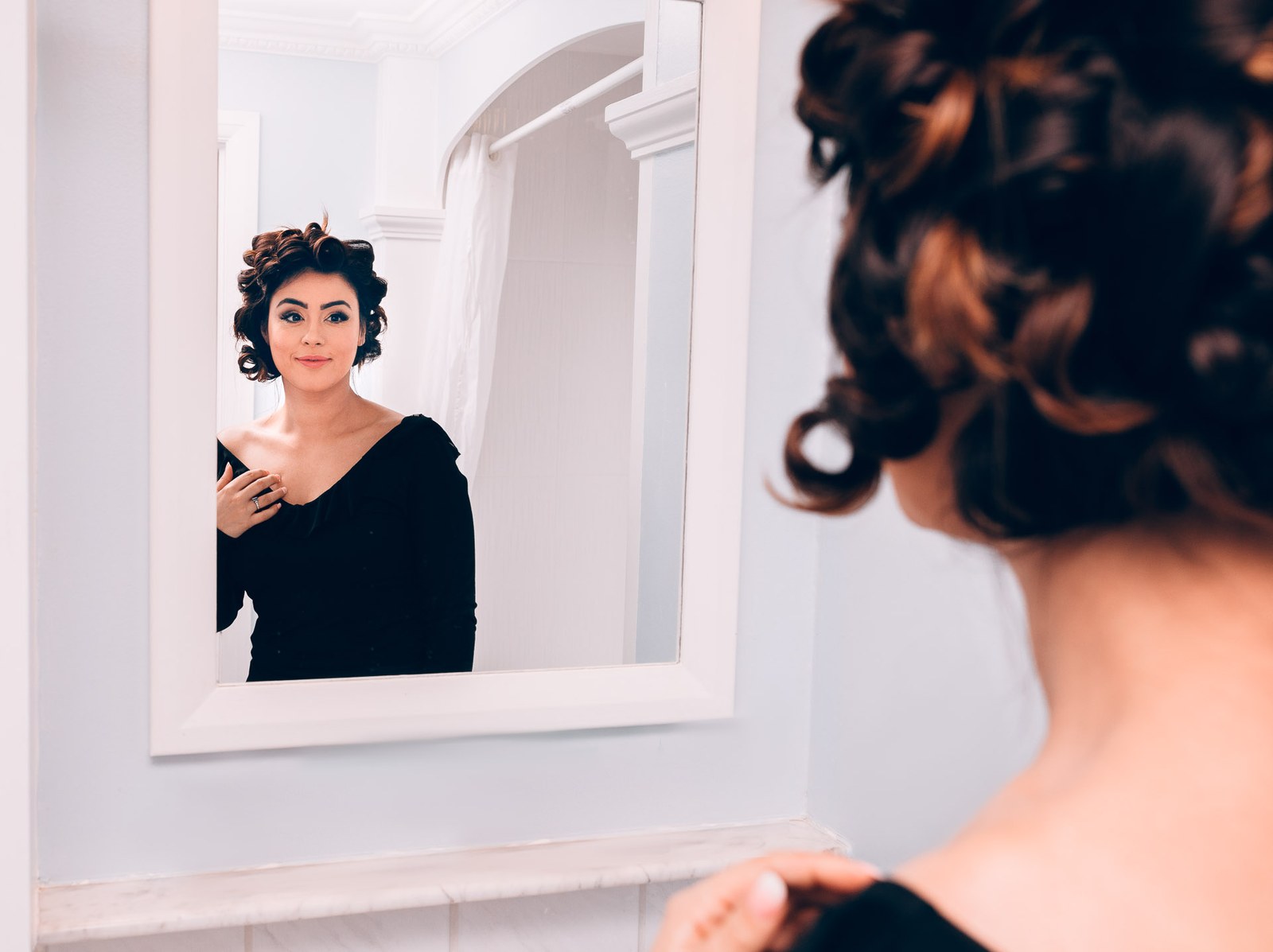 The bride in a black off-shoulder top checking her reflection in a mirror during preparations