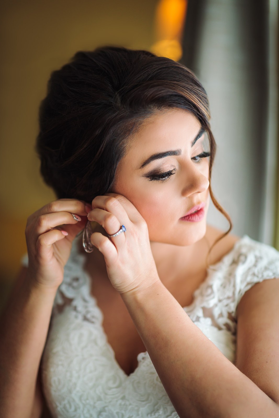 The bride fastening an earring, her lace gown already on