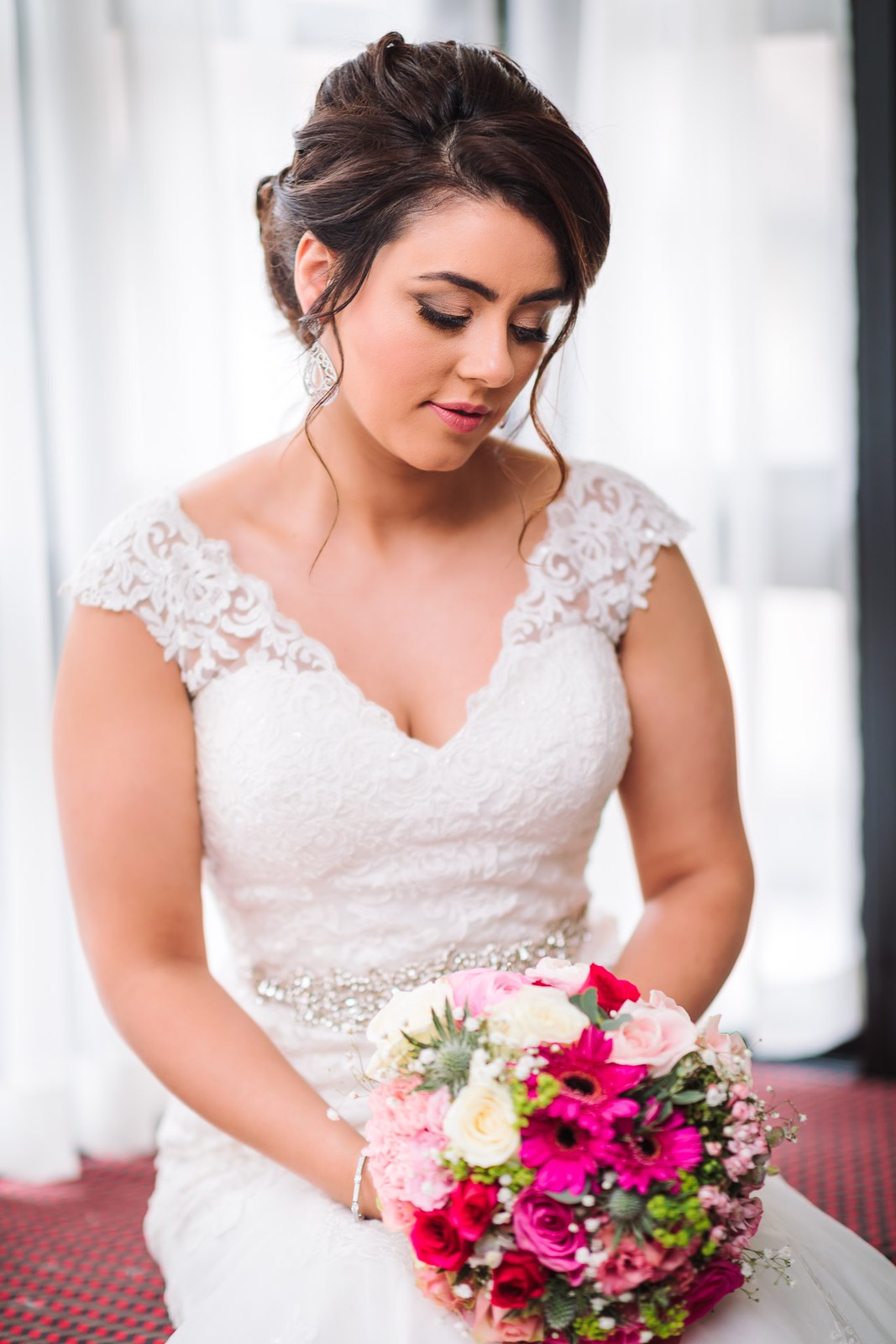 The bride looking down at her vivid pink and white bouquet by the window