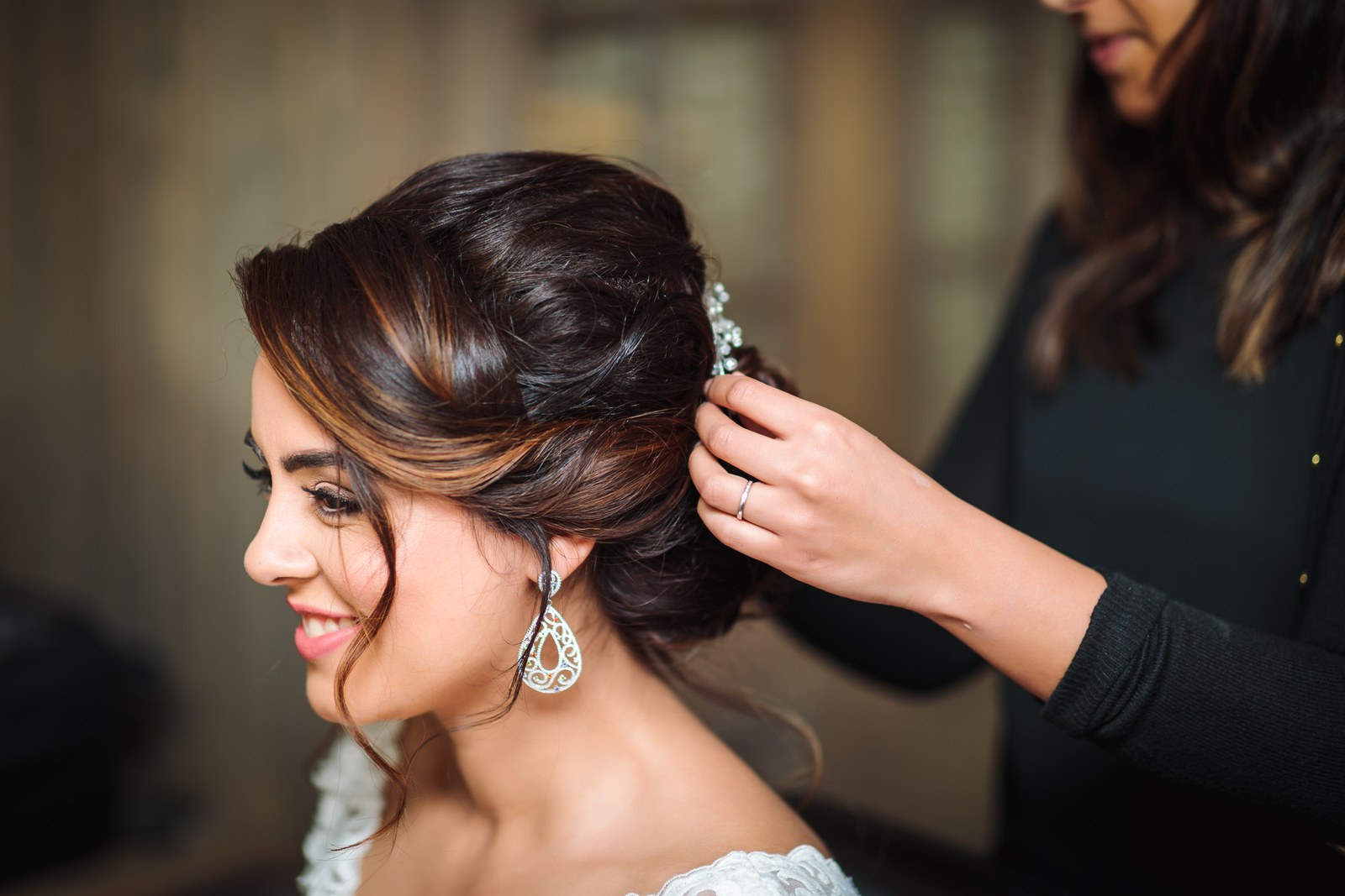 A stylist fixing a sparkling pin into the bride's updo, teardrop earrings catching the light
