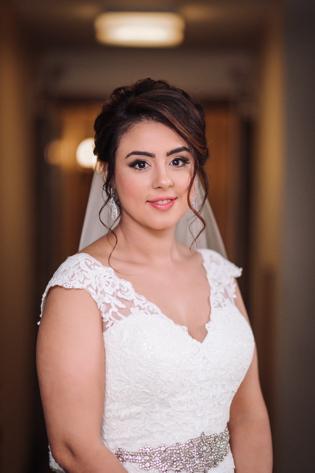 Portrait of the bride in her lace gown and jewelled belt, veil trailing