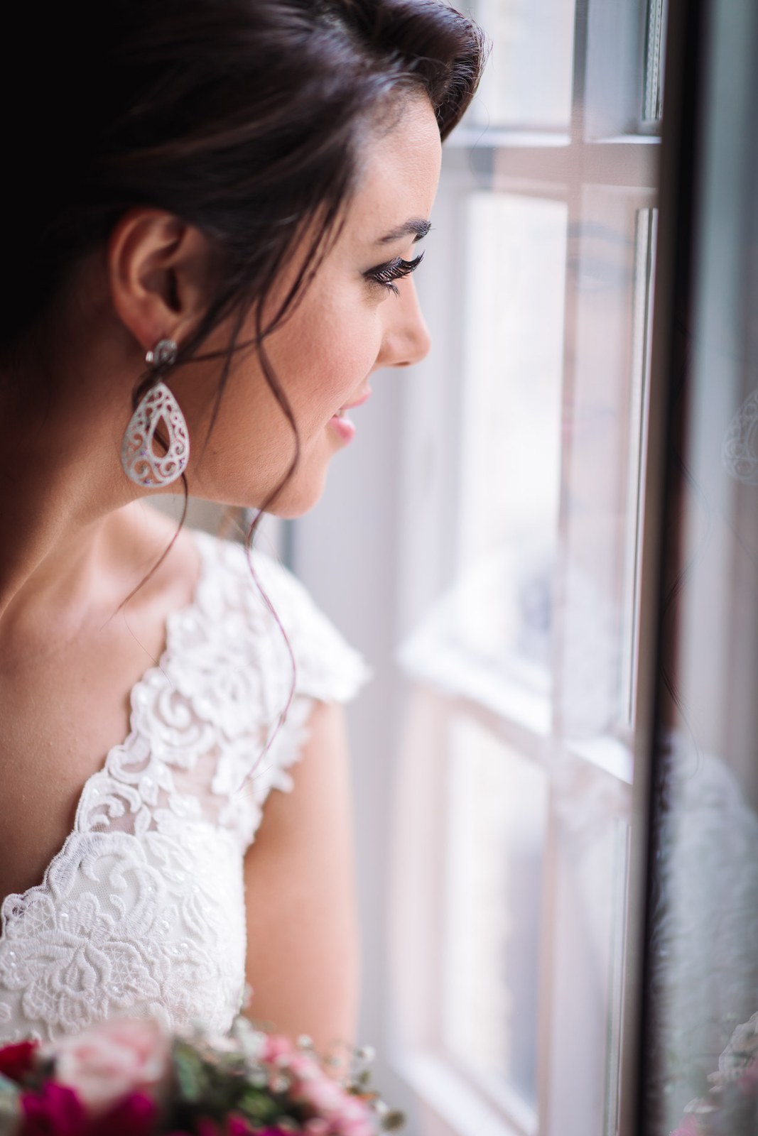 Profile of the bride by a window, a teardrop earring against her lace shoulder