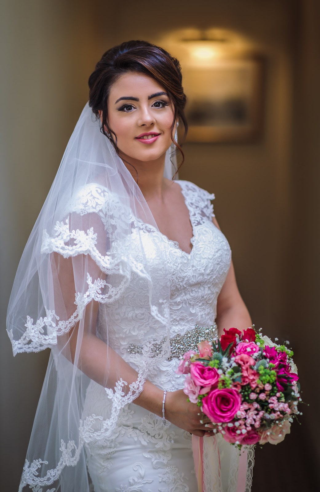 The bride holding her bright pink bouquet beneath a lace-edged veil