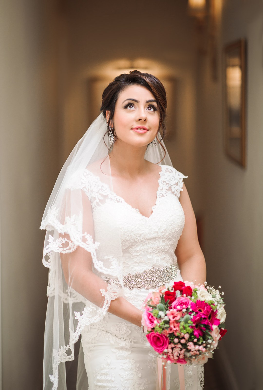 The bride glancing upward with her pink bouquet, veil framing her face