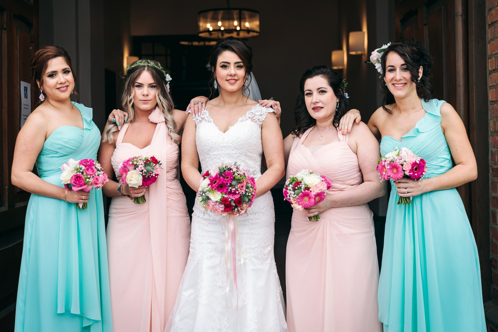 The bride flanked by bridesmaids in mint and blush gowns holding bouquets