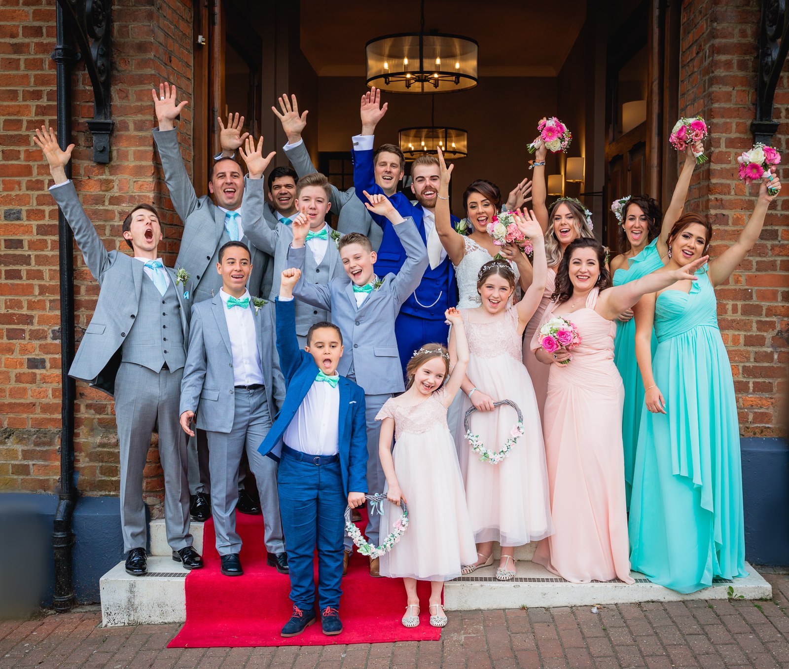 The whole wedding party cheering with arms raised on the steps of Villiers Hotel
