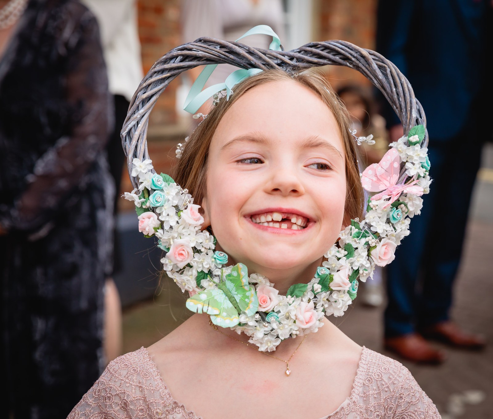A young flower girl grinning through a heart-shaped floral hoop
