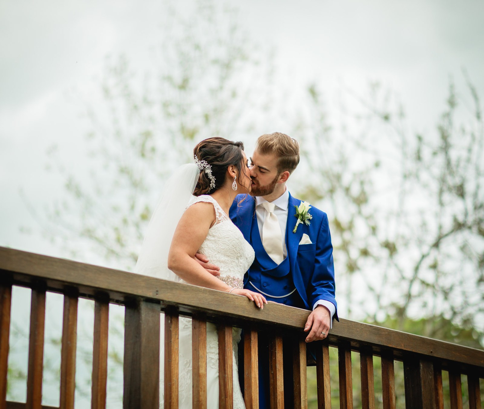 The couple kissing on a wooden footbridge in a riverside park