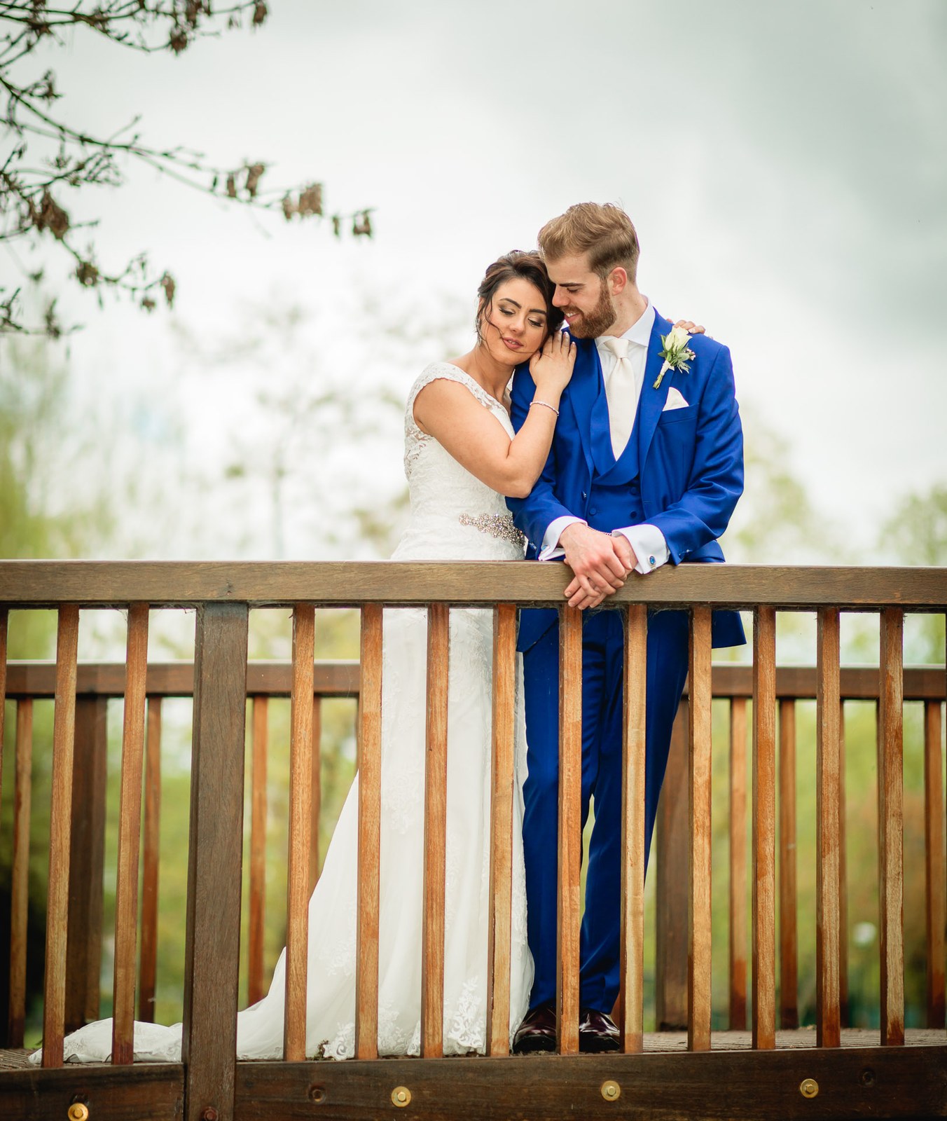 Bride and groom leaning on the wooden bridge rail against a bright open sky