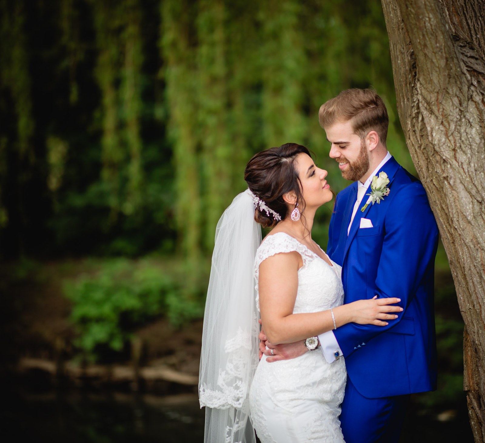 The couple embracing beneath a weeping willow beside the water