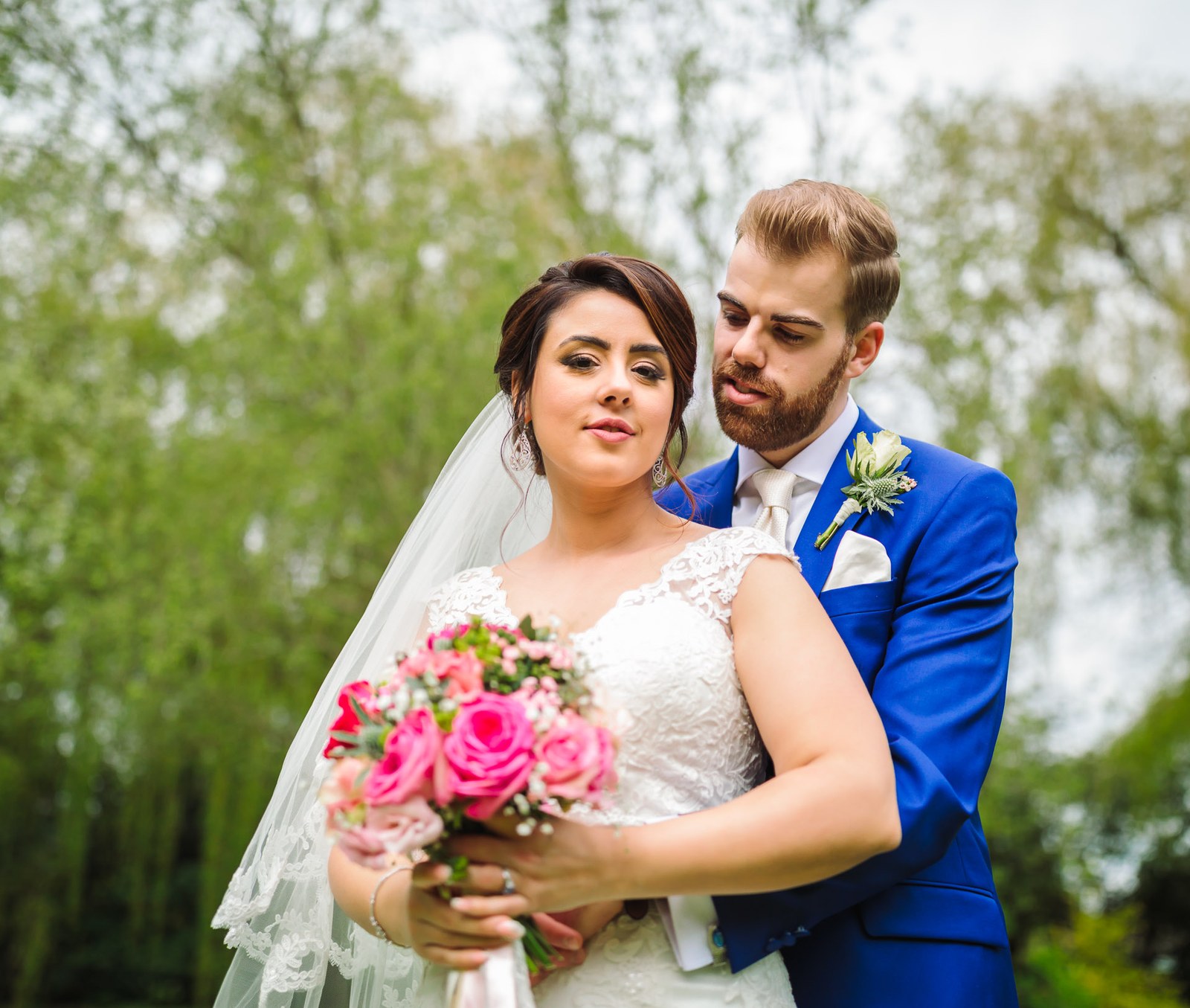 The couple embracing under the willow, the bride holding her pink rose bouquet