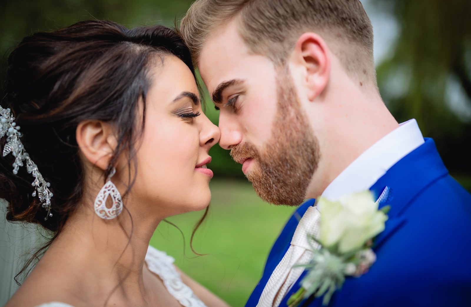Foreheads together, the bride's teardrop earrings sparkling against the groom's blue suit