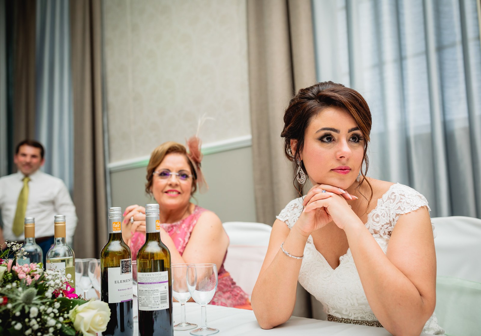 The bride resting her chin on her hands at the top table beside a guest in coral