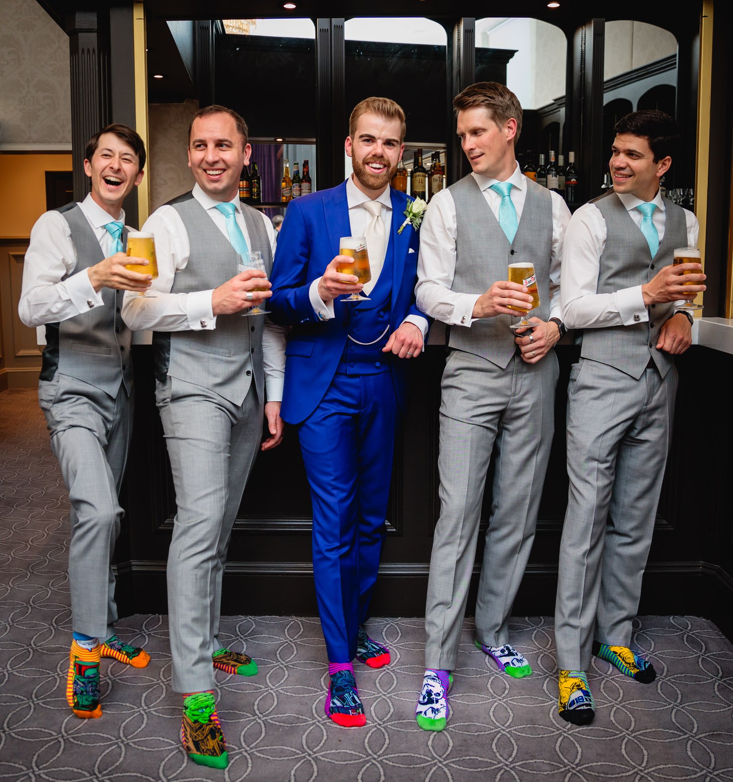 The groom and groomsmen showing off colourful novelty socks at the hotel bar