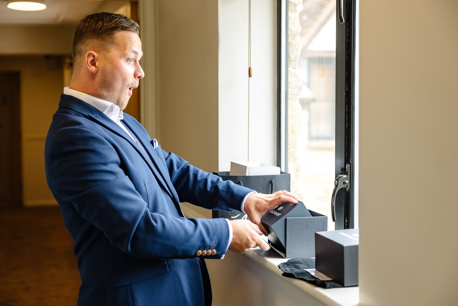 Groom opening a gift box on the windowsill while getting ready