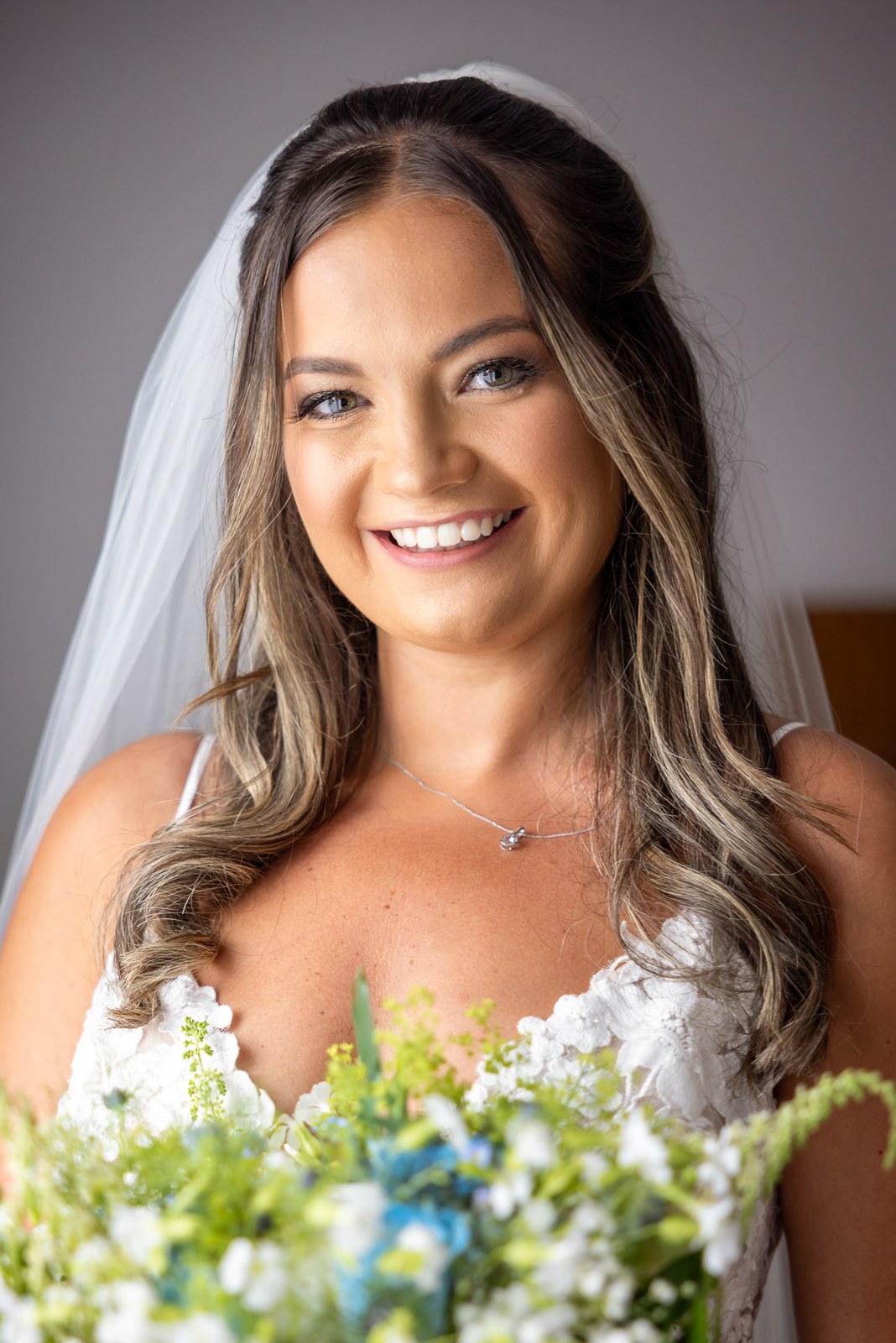 Bride smiling with her bouquet, veil softly framing her face