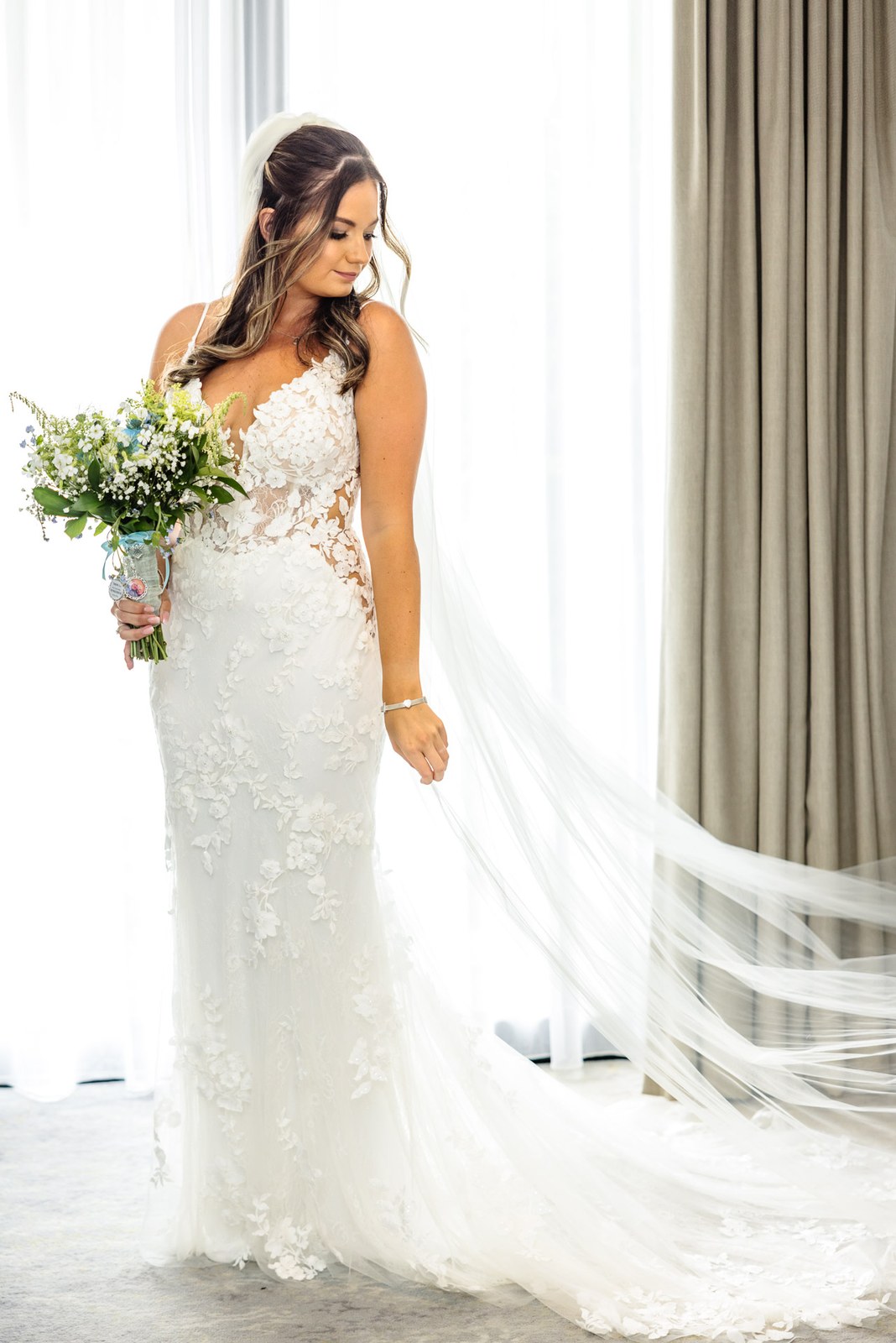 Bride posing with her long veil train and bouquet by the window