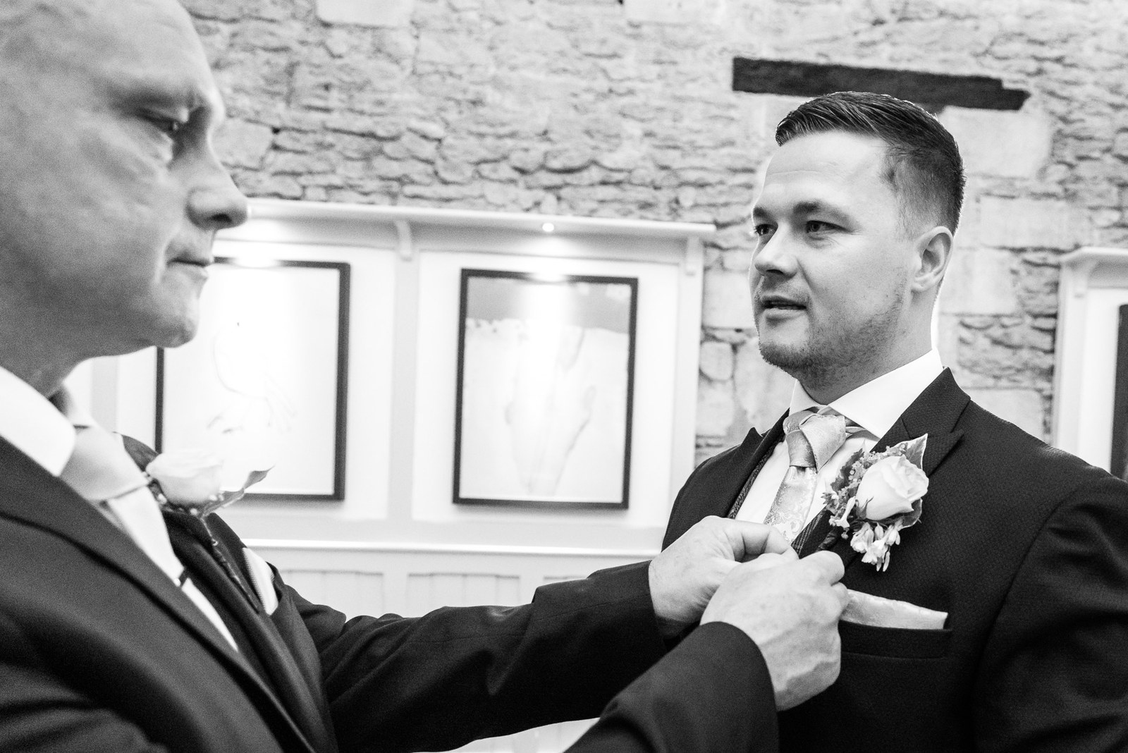 Buttonhole being pinned to the groom's lapel in black and white