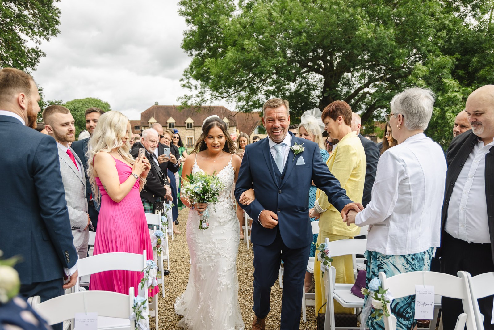 Bride escorted down the outdoor aisle by her father past standing guests