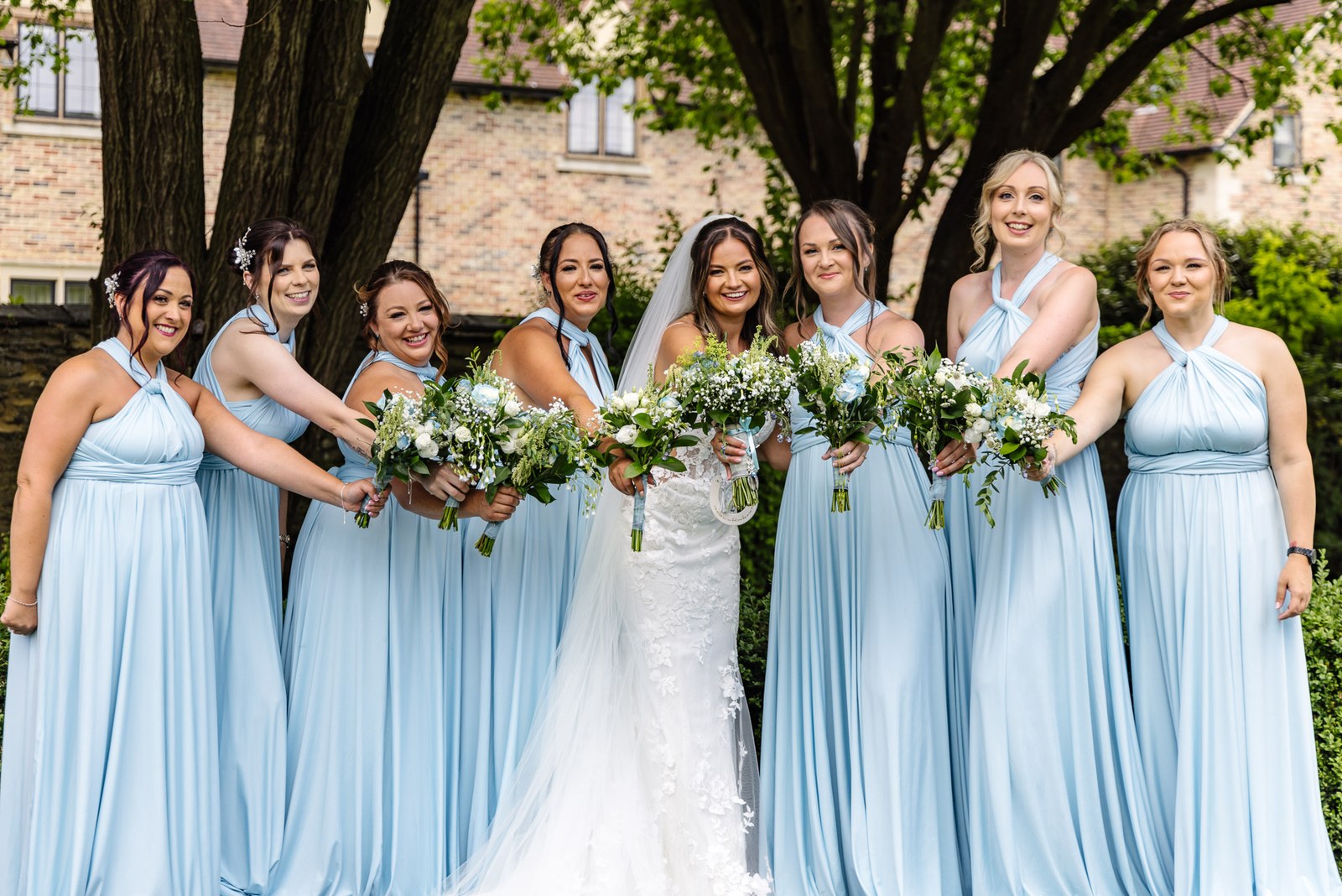 Bride and bridesmaids with bouquets beneath a tree at voco Oxford Thames