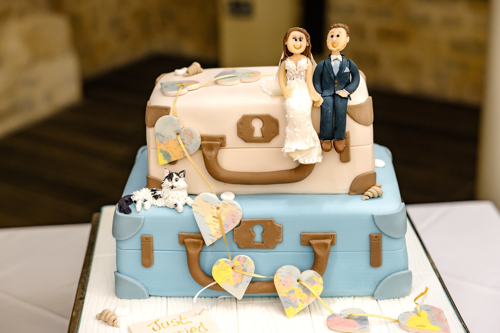 Two-tier wedding cake styled as vintage suitcases with figurine toppers