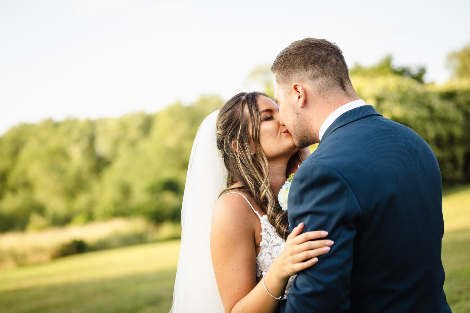 Newlyweds kissing with open countryside stretching behind them