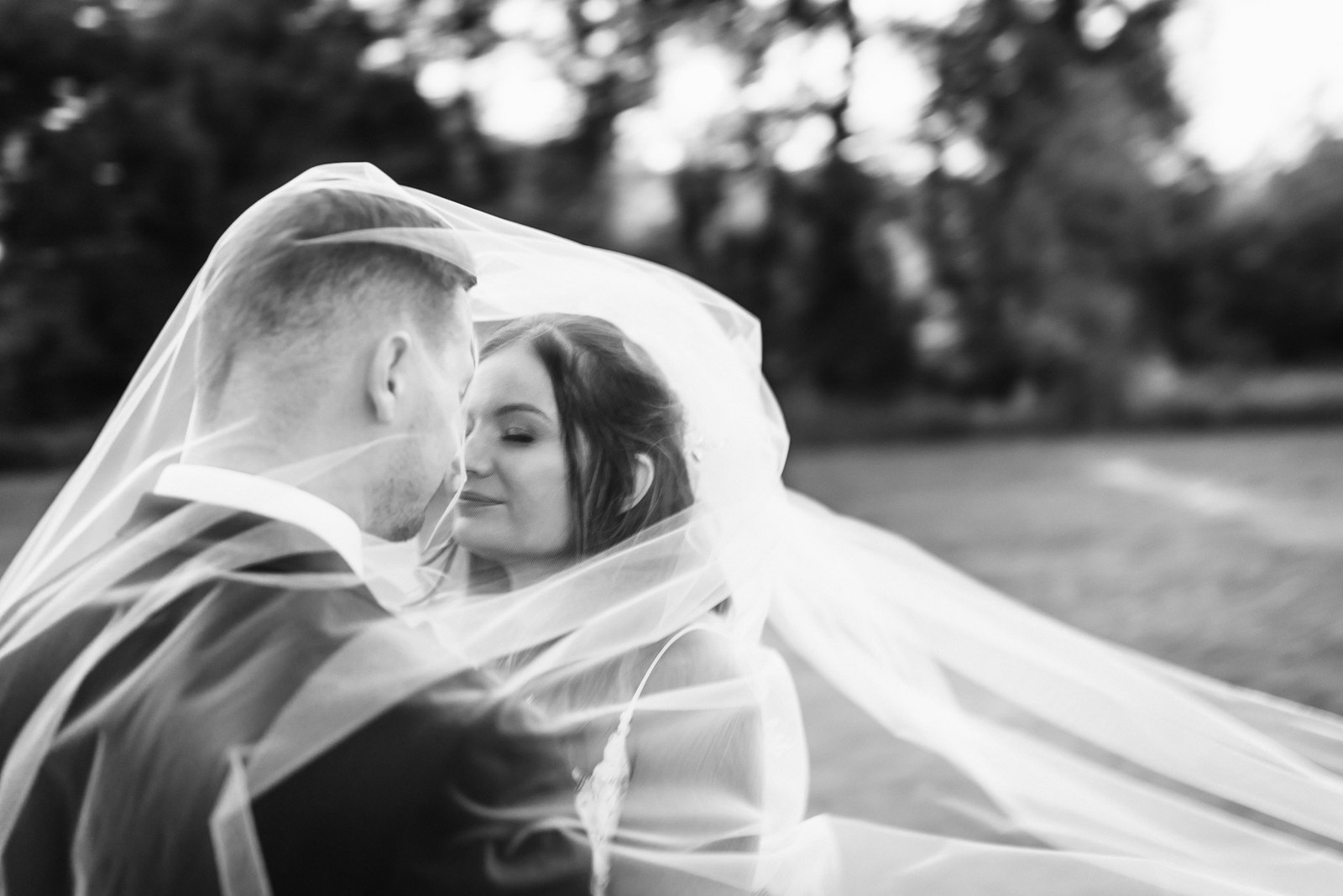 Black and white portrait of the couple beneath the veil by the water