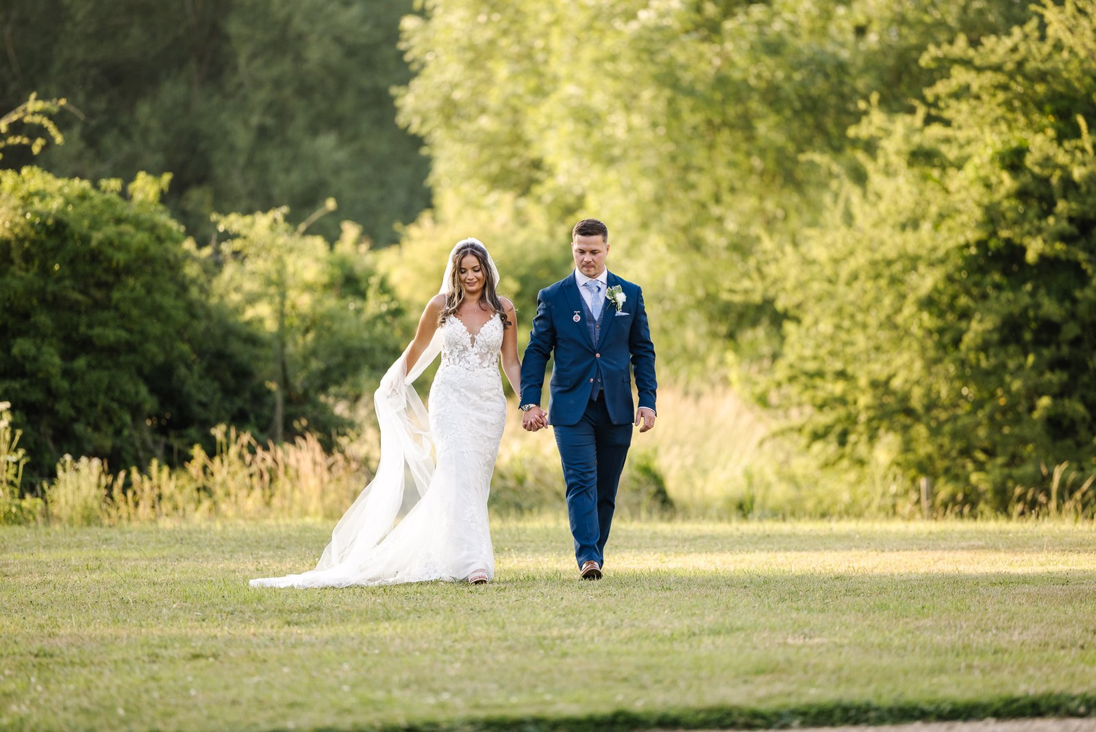 Newlyweds strolling through a golden meadow at sunset