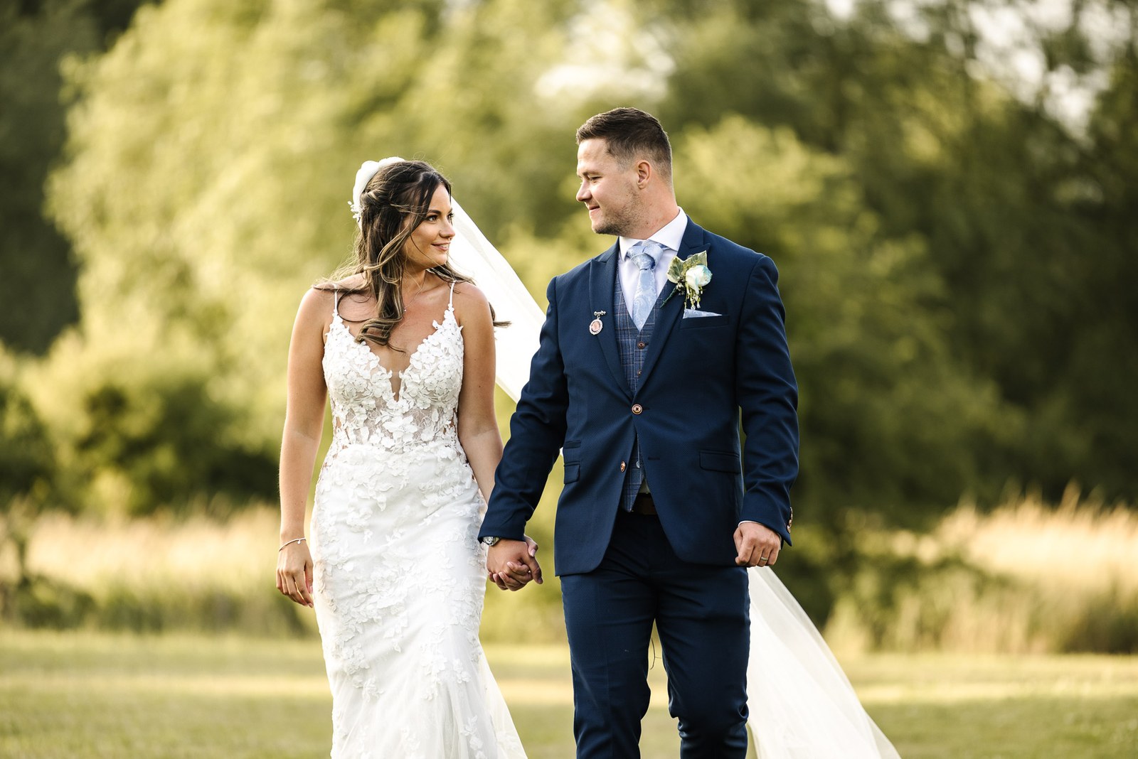 Bride and groom walking hand in hand through tall summer grasses