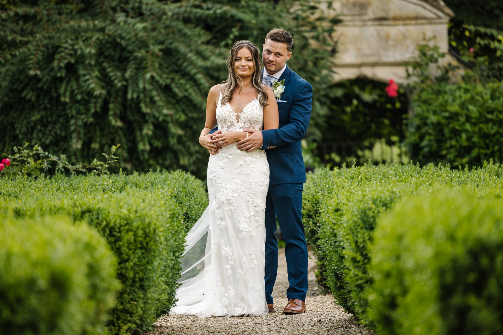 Newlyweds embracing on a hedge-lined path at voco Oxford Thames