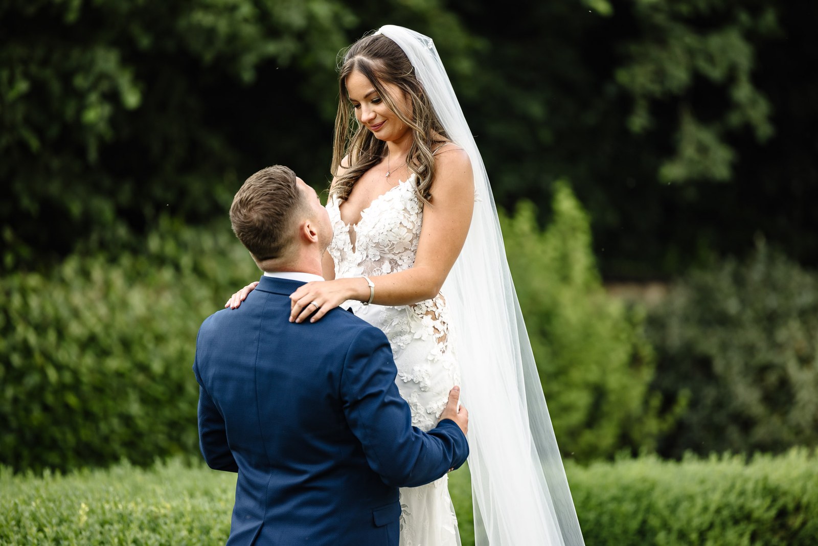 Groom embracing the veiled bride among the clipped garden hedges