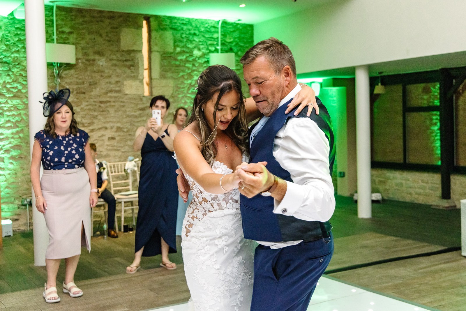 Bride dancing with her father under green lighting on the dance floor