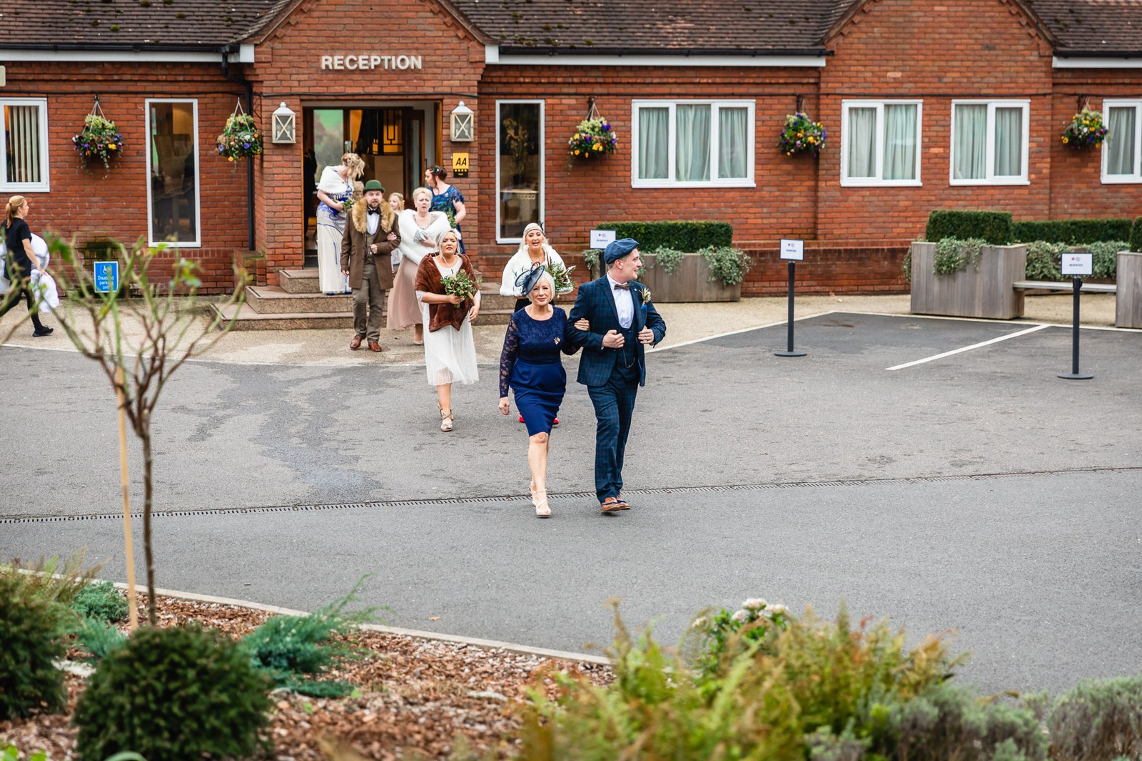 A groom and guests walking from the red-brick reception entrance of Windmill Village Hotel