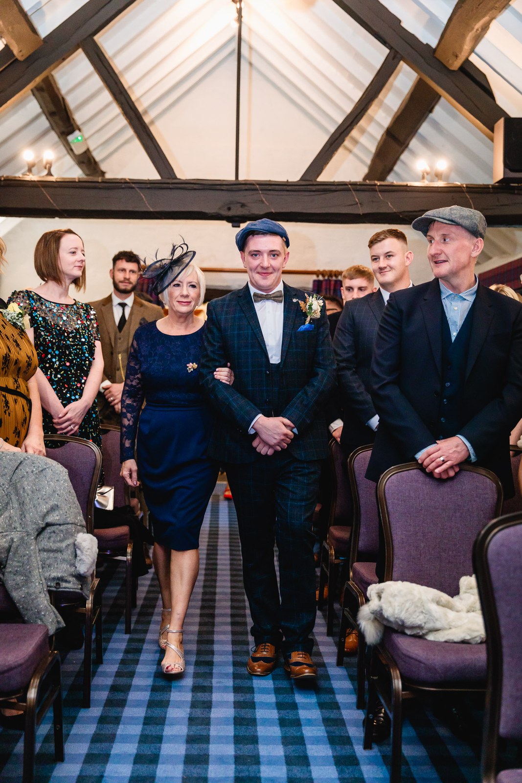 A groom walking down the aisle in the beamed ceremony room at Windmill Village Hotel