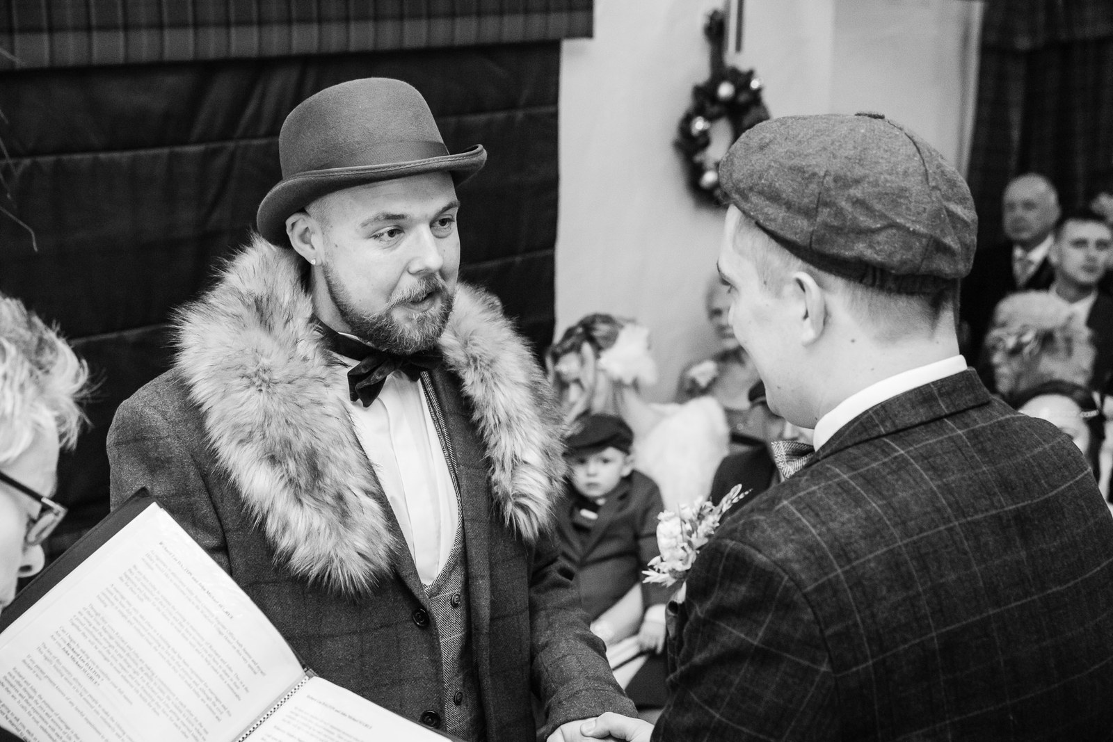 The grooms exchanging vows in black and white, one wearing a bowler hat