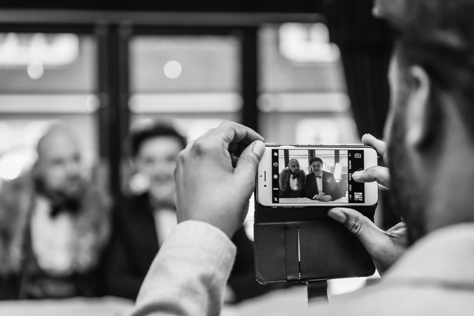 A guest capturing the ceremony on a phone, in black and white