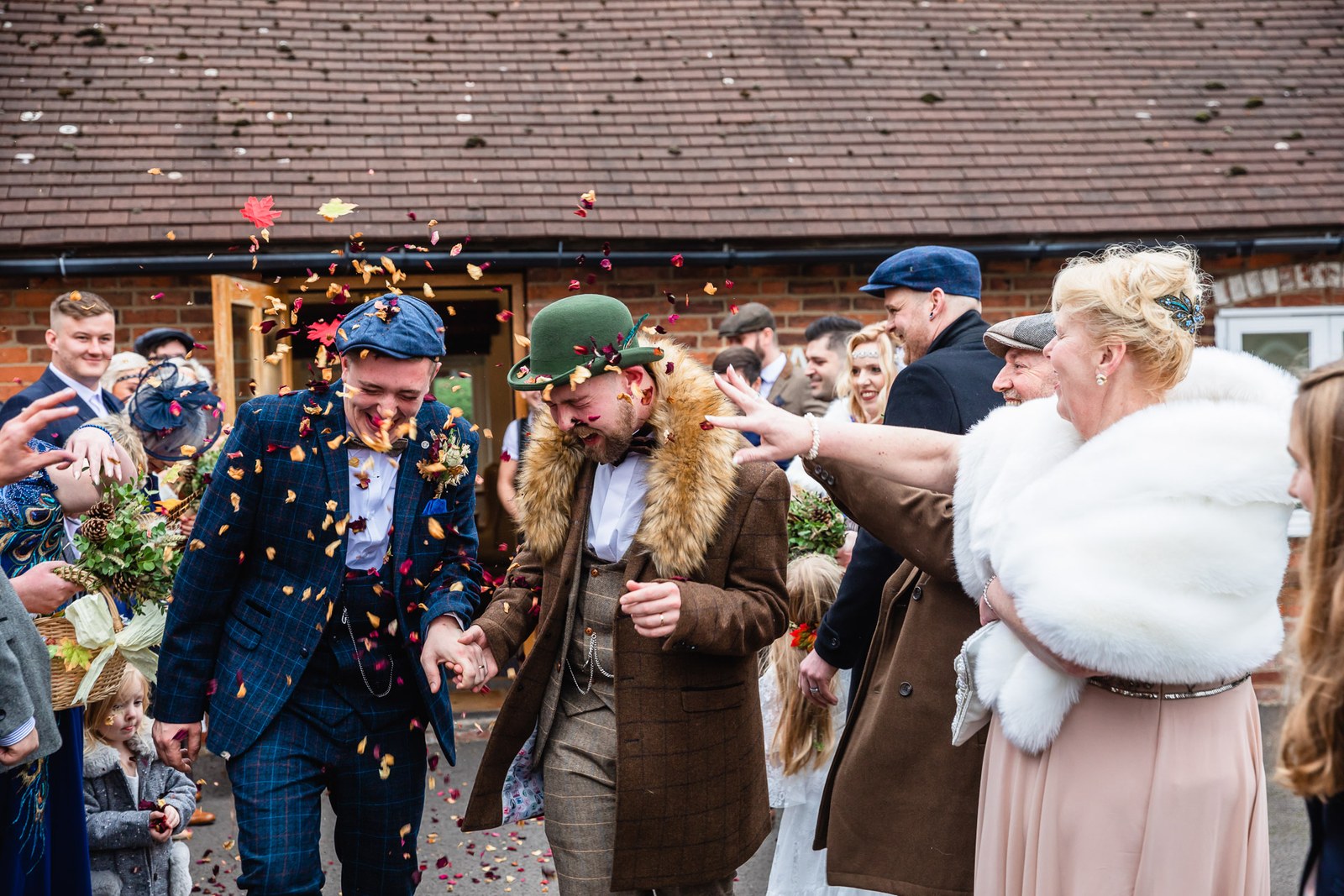 The grooms passing through a confetti tunnel outside the venue