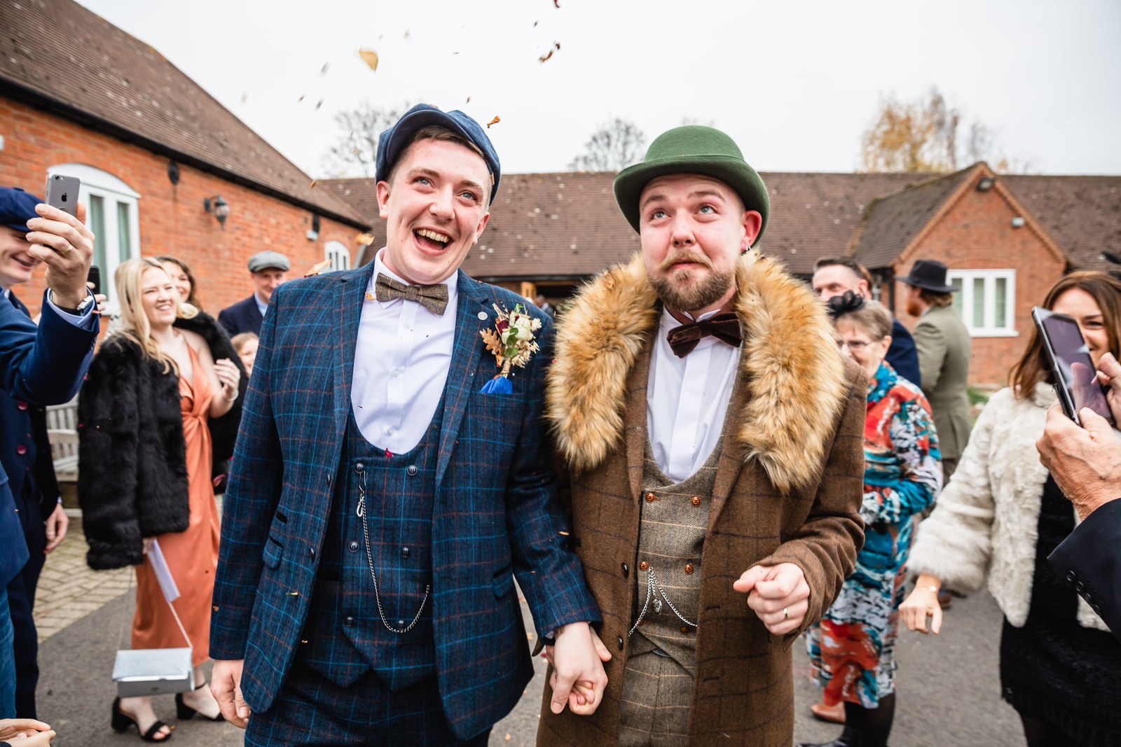 The two grooms walking through confetti as guests film them