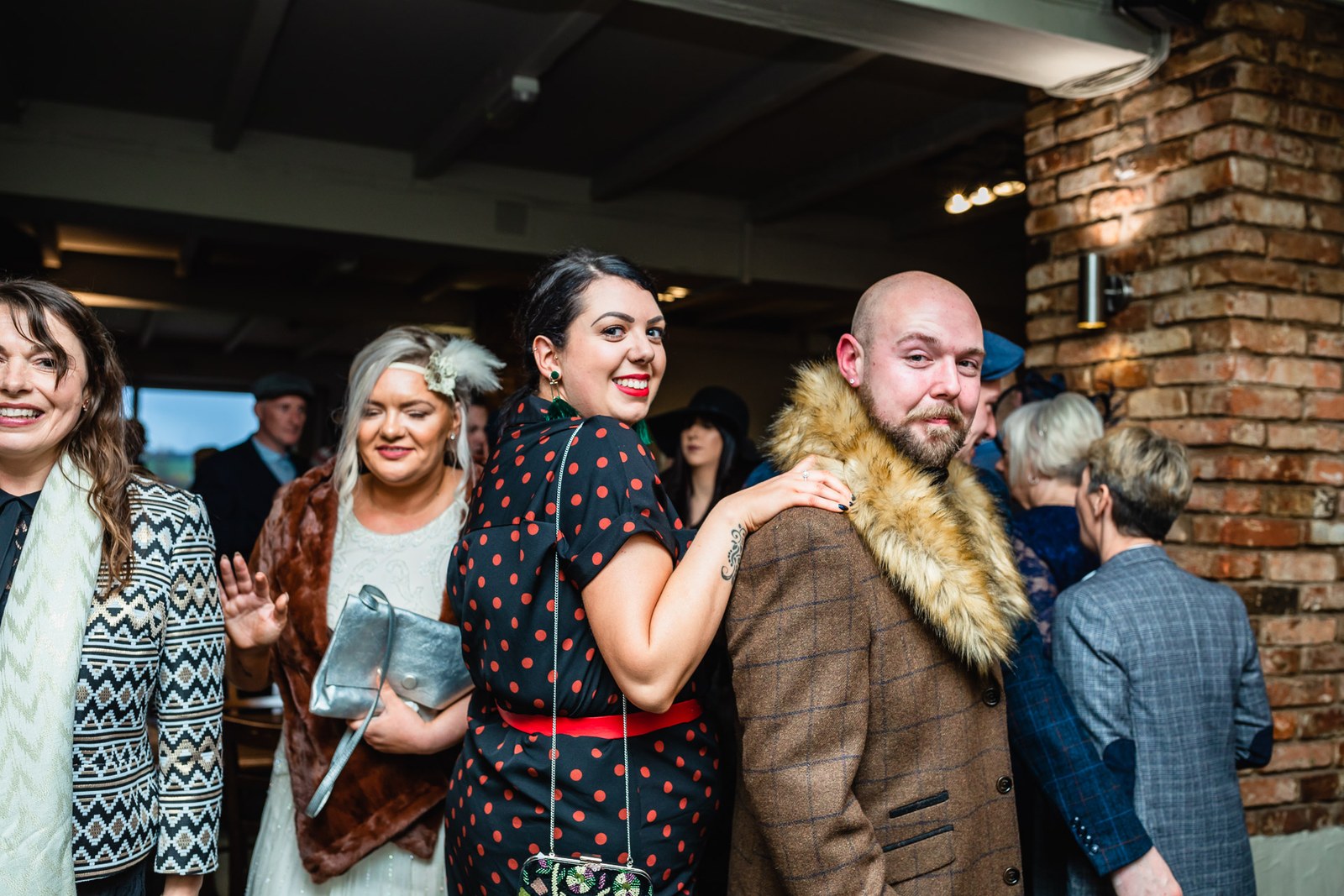 A groom and guests mingling beside the exposed brick wall at the reception
