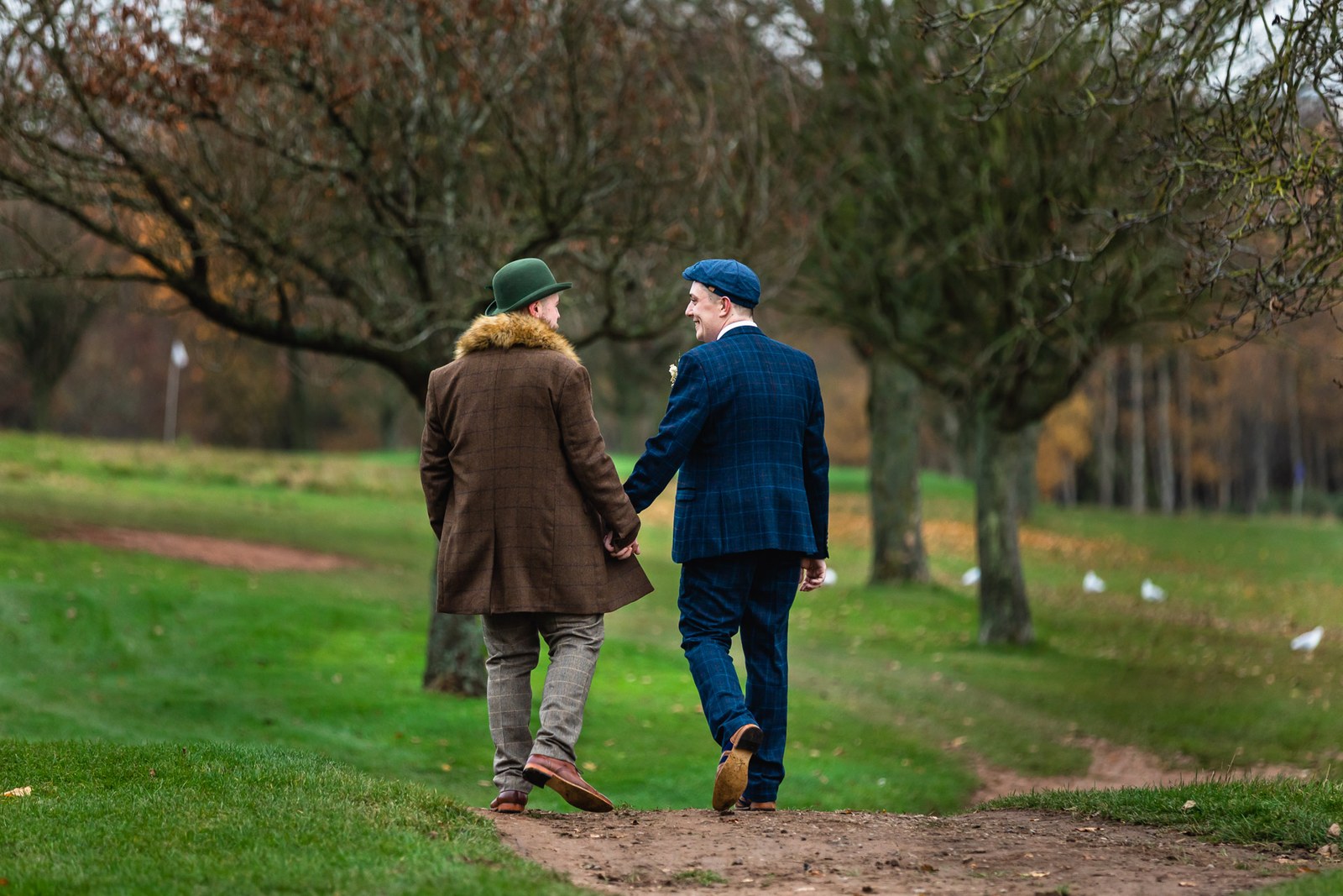 The grooms walking hand in hand across the Windmill Village Hotel grounds in autumn