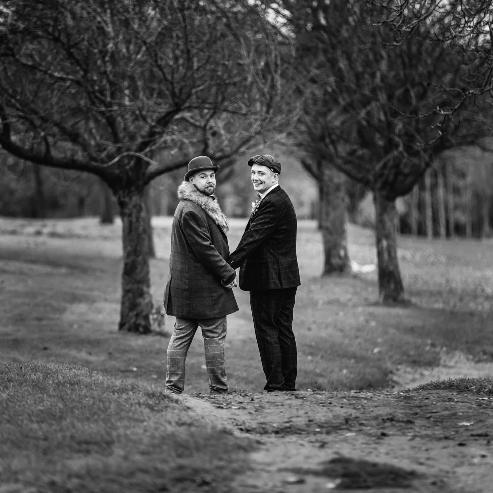 Black and white portrait of the grooms holding hands among bare trees