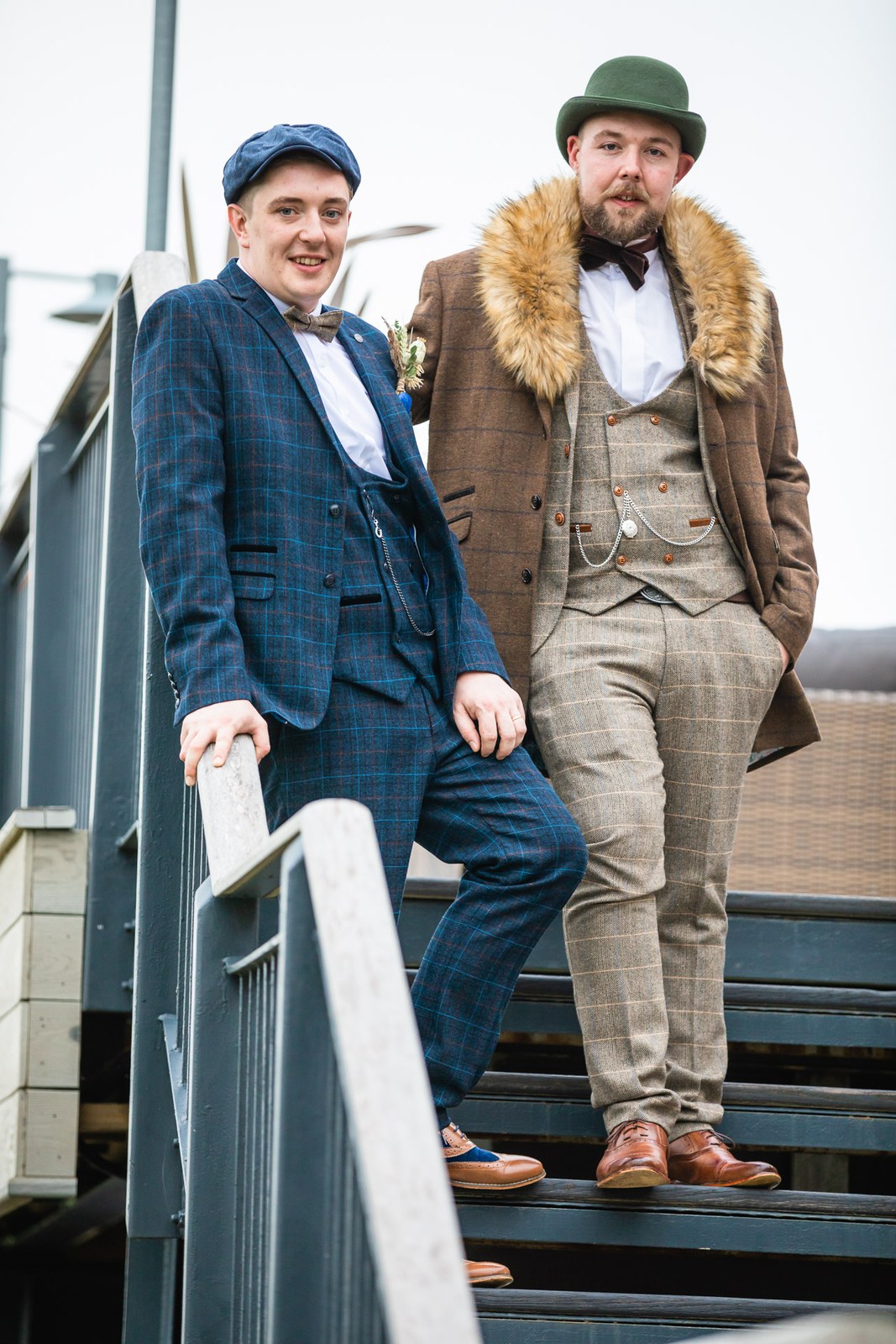 The two grooms posing together on a footbridge with metal railings