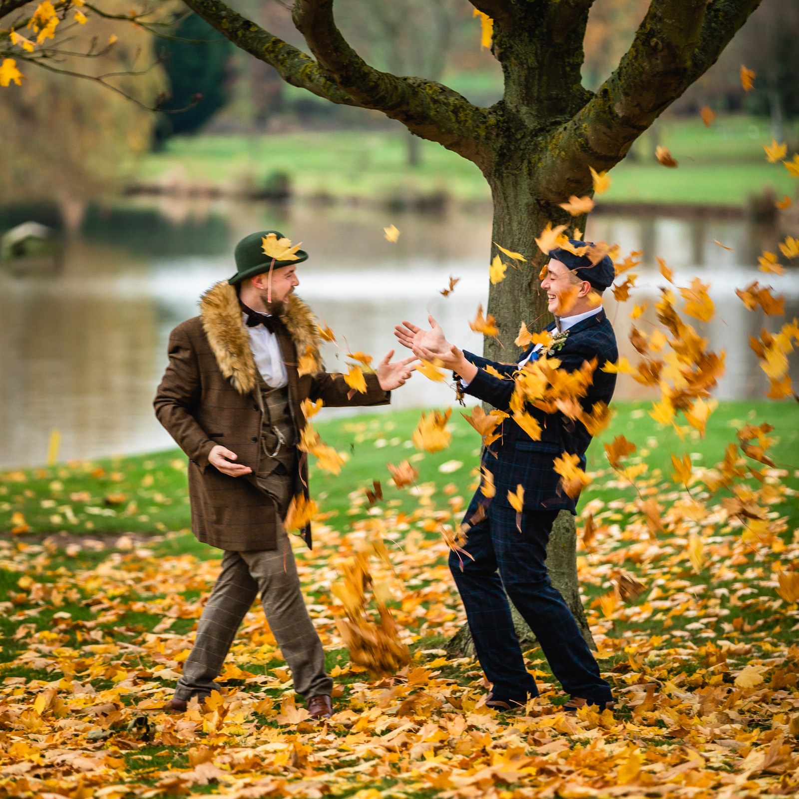 The grooms tossing armfuls of autumn leaves by the lake