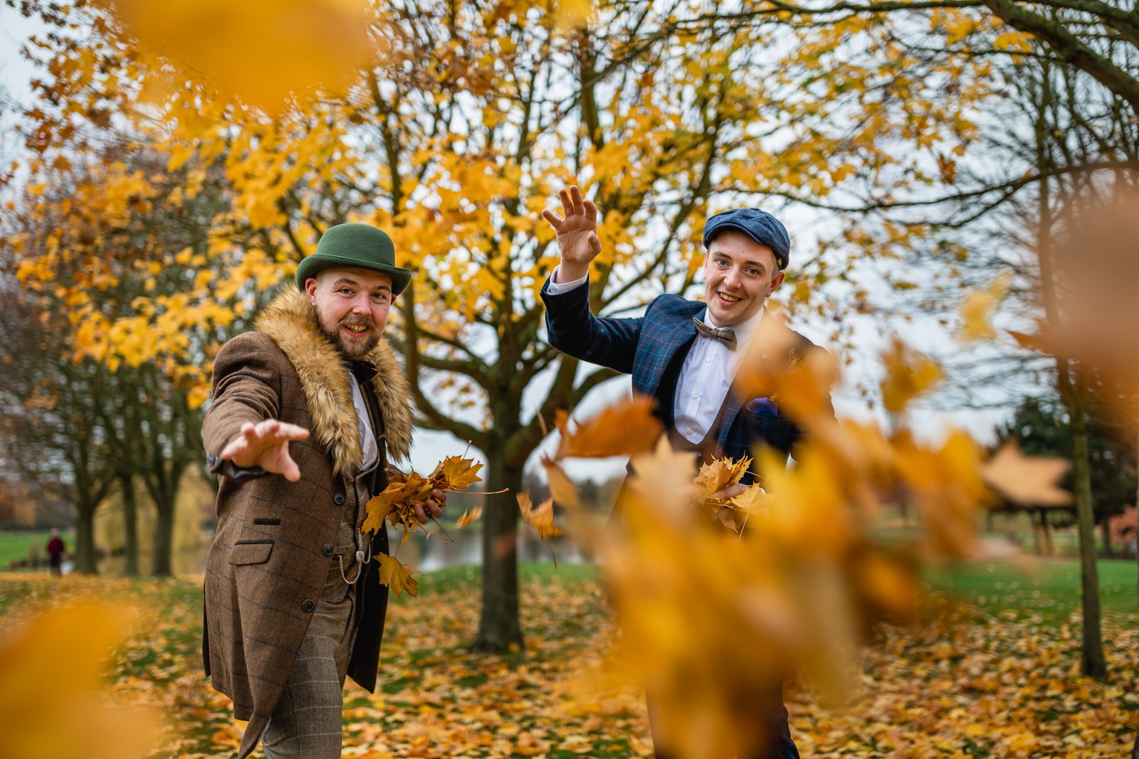 The grooms playfully throwing golden leaves beneath a tree