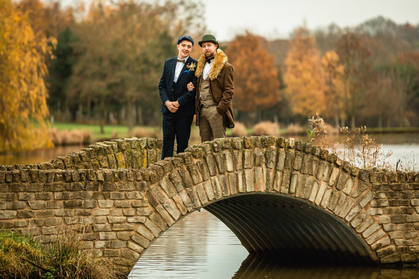 The two grooms standing on the stone arched bridge over the lake